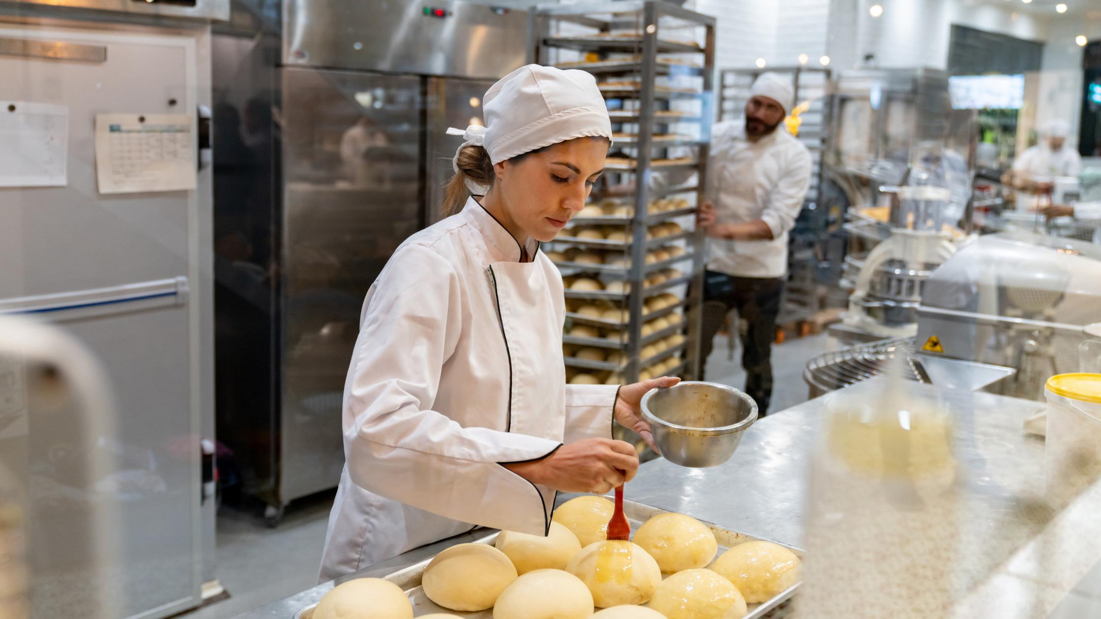 Female baker spreading egg yolks on bread at the bakery