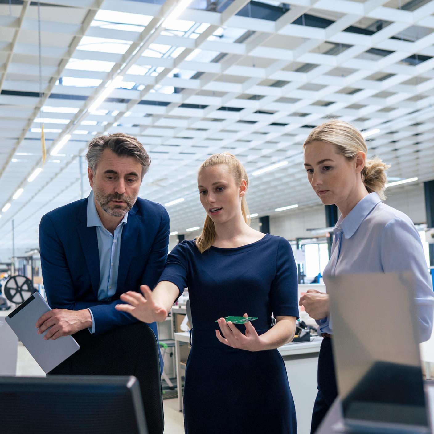 Young businesswoman with colleagues discussing over computer at factory