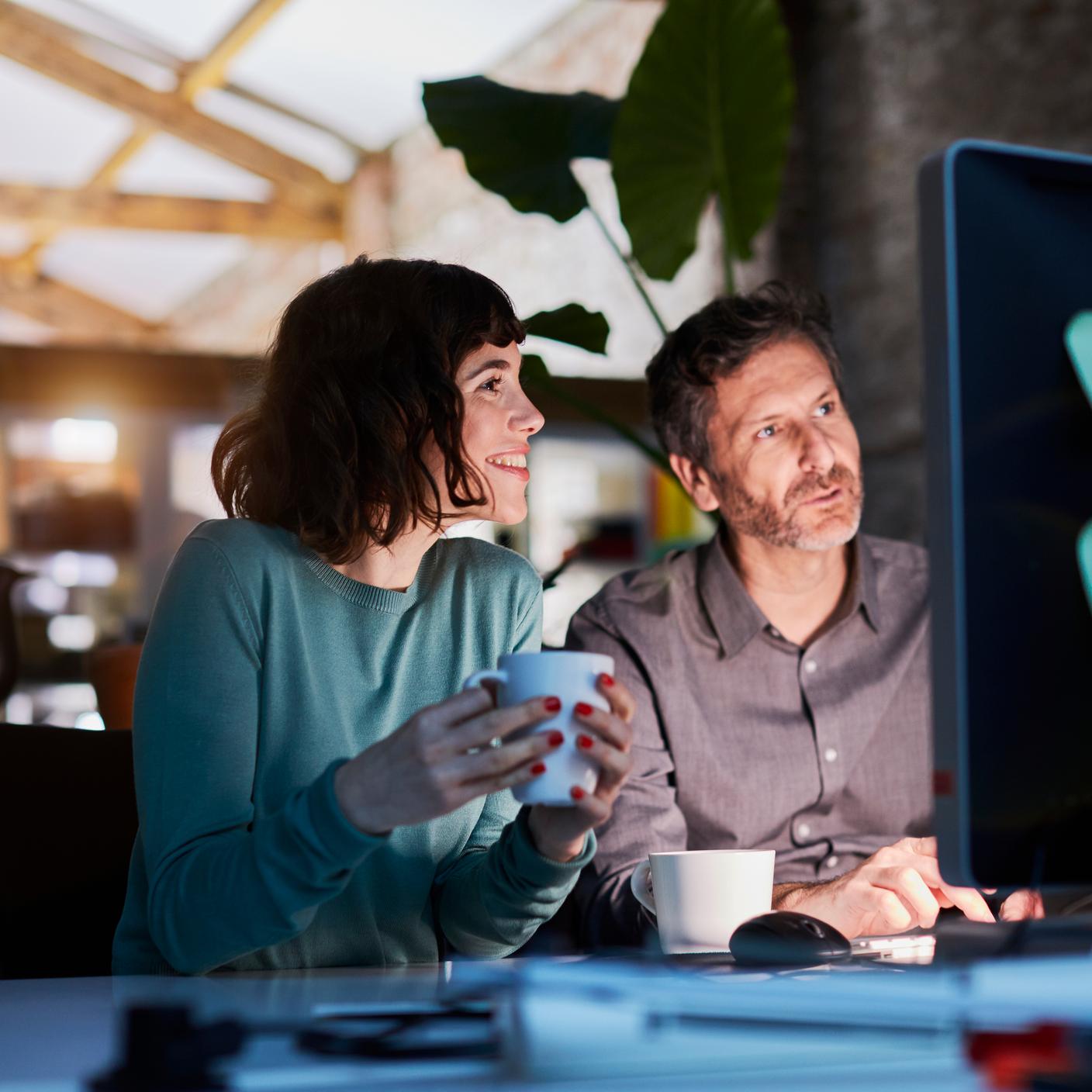 Two people sitting at a desk both looking at a screen having a discussion