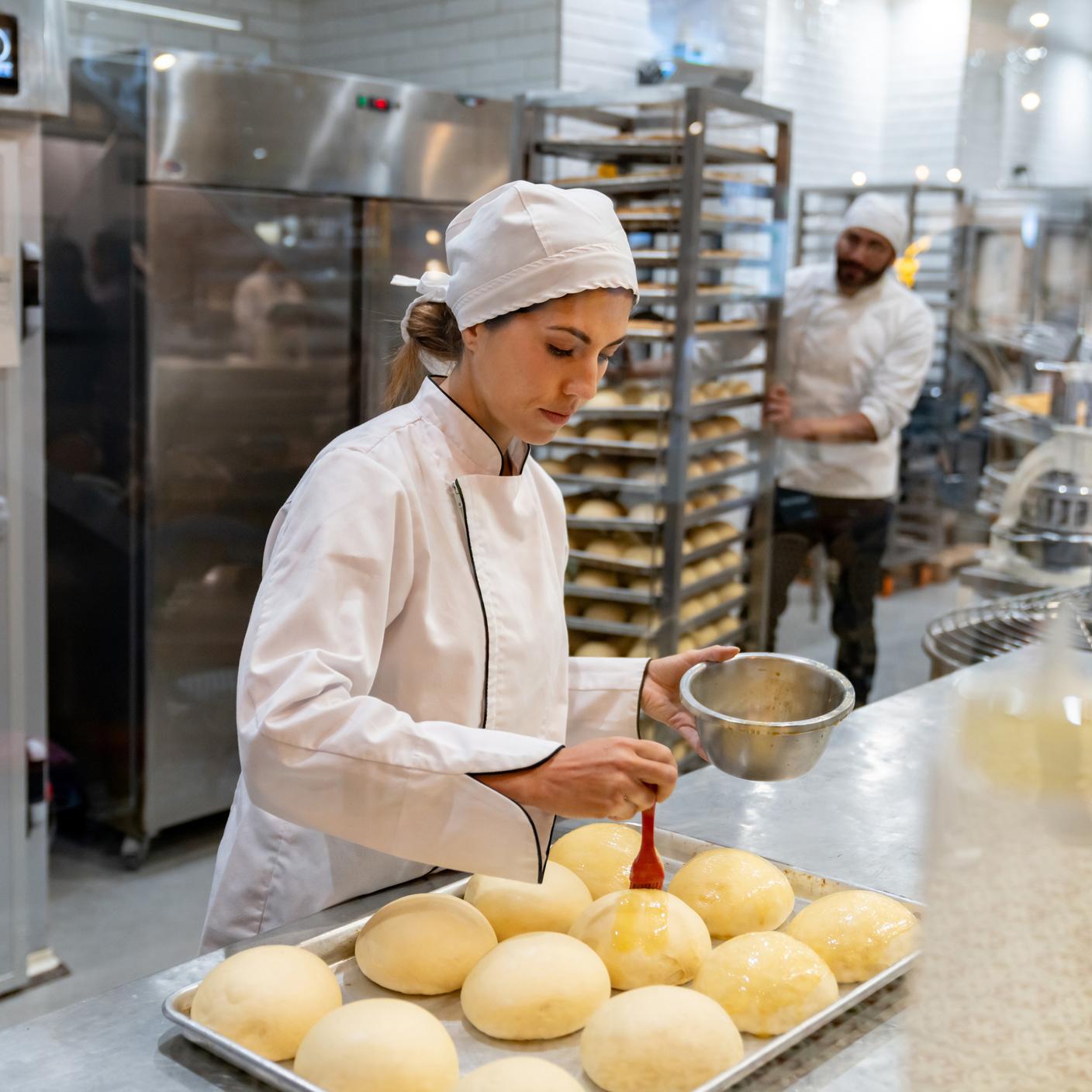 Female baker spreading egg yolks on bread while baking at the bakery