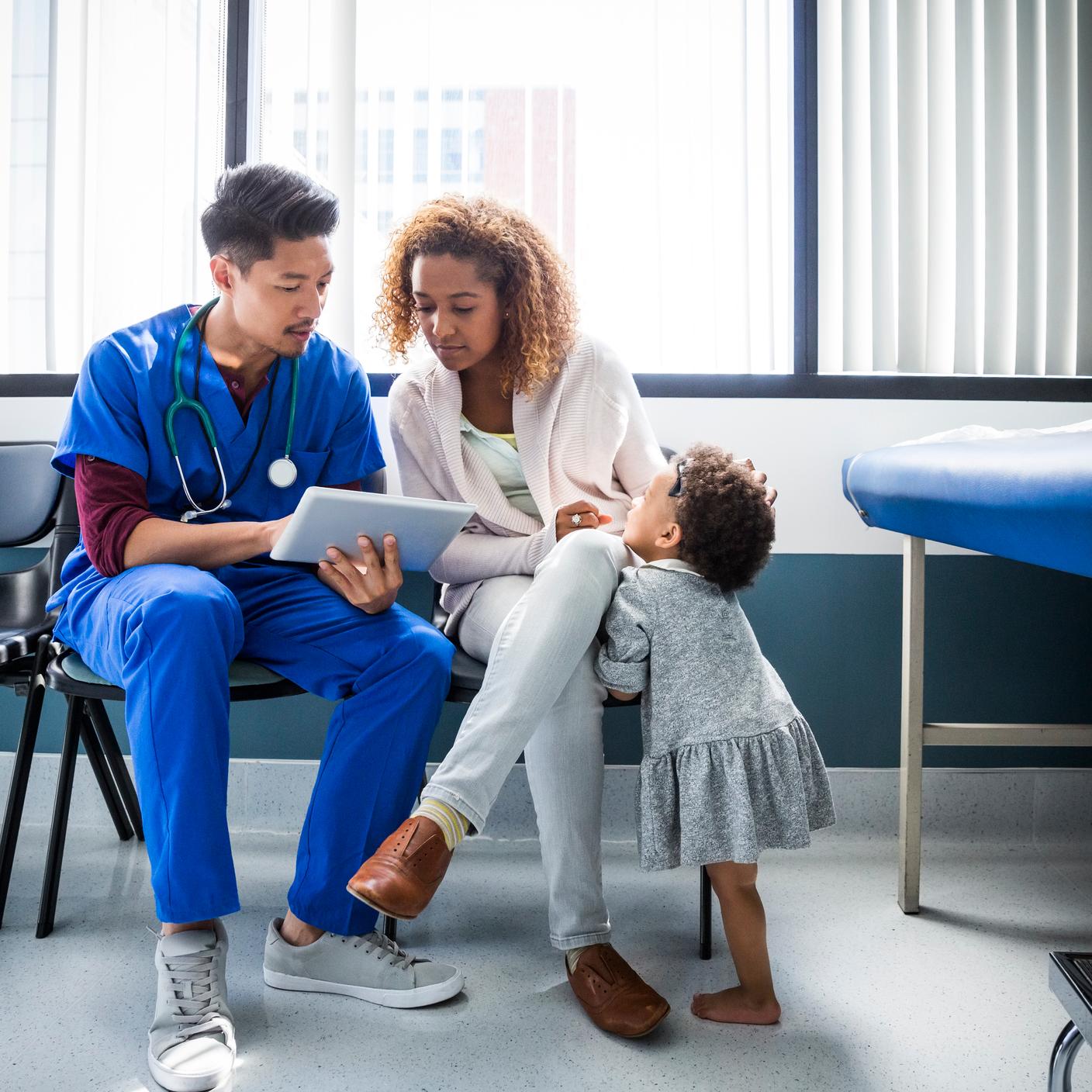 Male nurse showing digital tablet to mother by toddler in hospital.