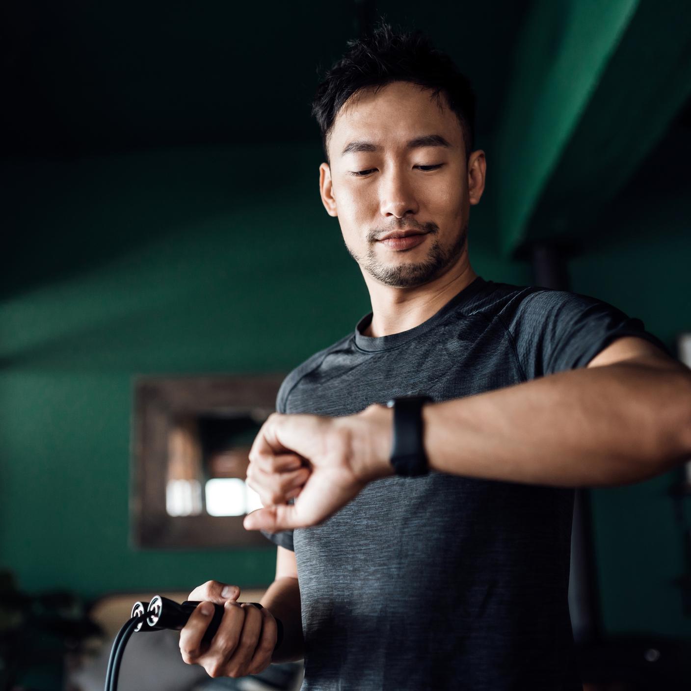 Active young Asian man exercising at home, using fitness tracker app on smartwatch