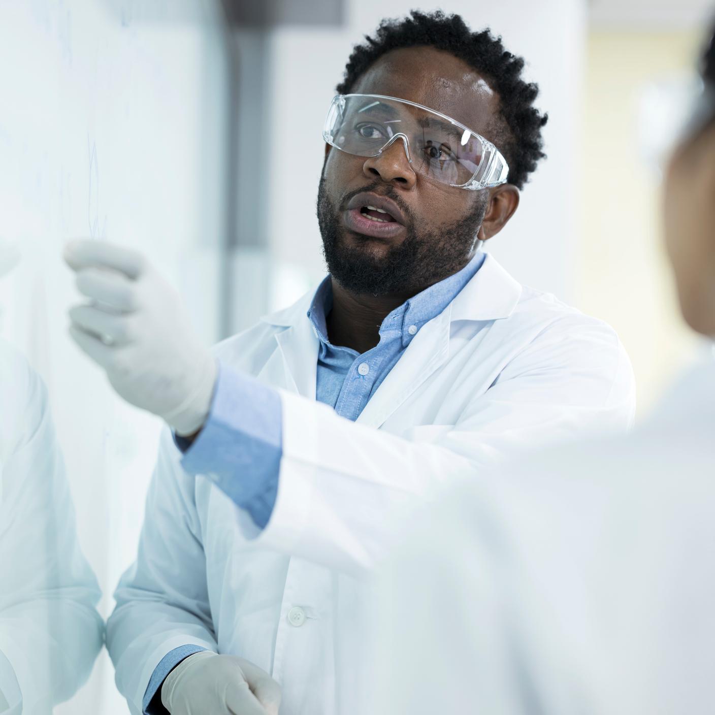 Efficiency over thoroughness in laboratory testing decision. Male African American scientist leading discussion of experiment with colleagues at white board in laboratory