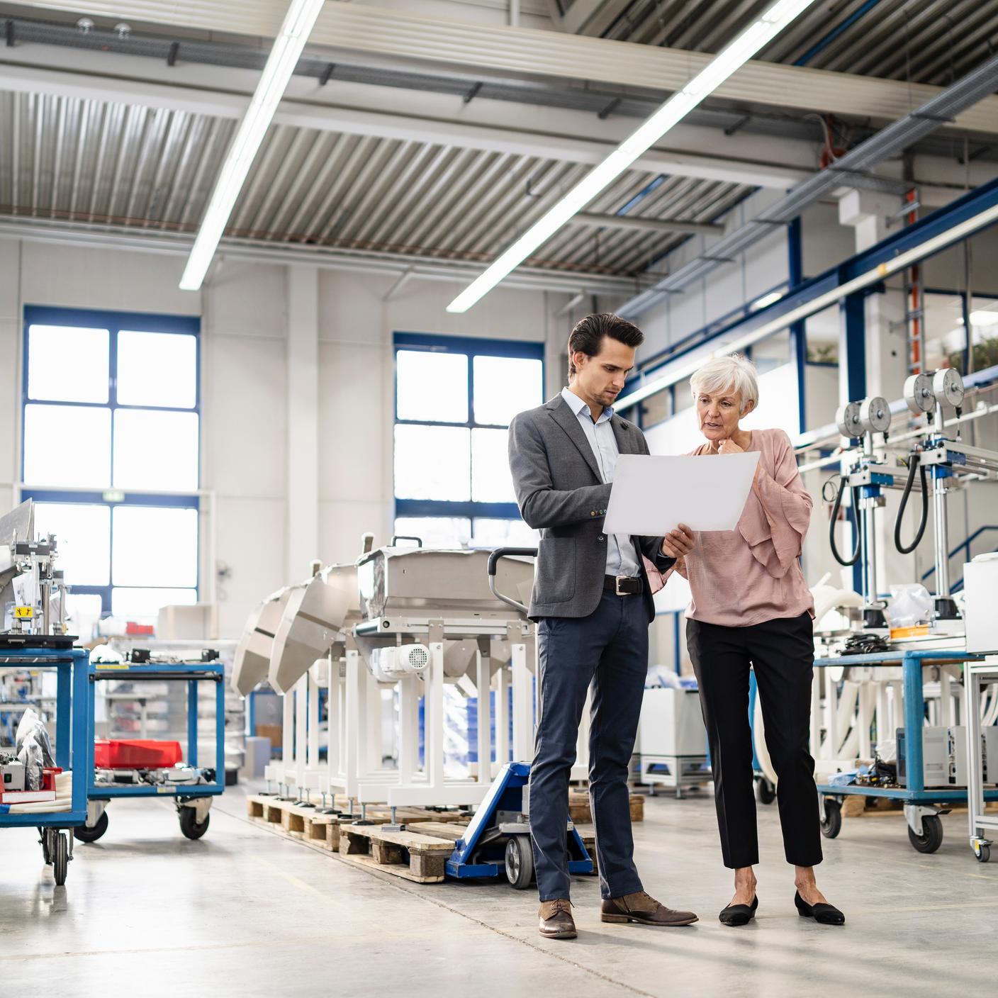 Businessman and senior woman looking at plan in a factory