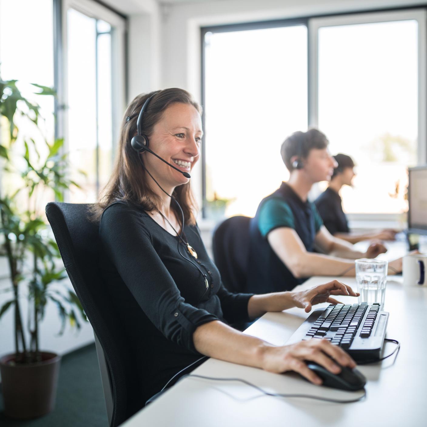 Smiling female customer service representative wearing headset using computer at desk in office