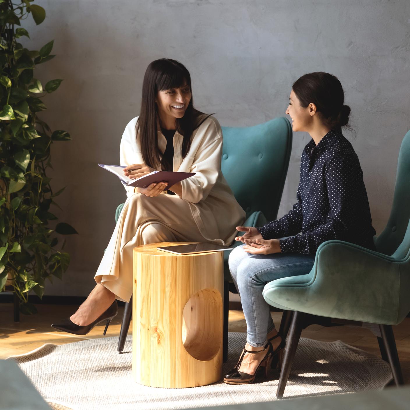 Deux collègues sympathiques, assises dans des fauteuils, discutent et échangent des informations lors d’une réunion informelle dans le hall d’entrée moderne d’un bureau. Conversation entre une femme d’affaires d’origine indienne et une femme d’affaires caucasienne au cours d’un flux de travail (recadré)