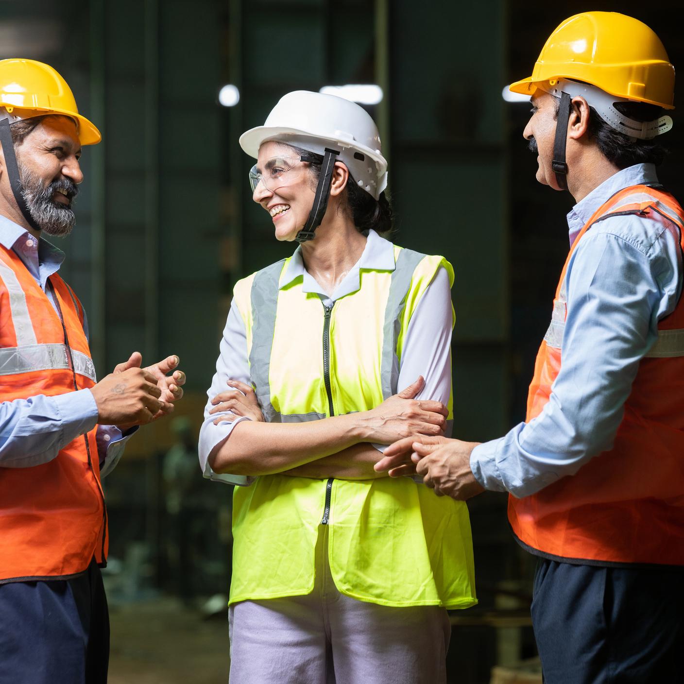 Team of happy indian engineers wearing safety hard hat and vest laughing and talking at industrial factory, skill india concept. Closeup