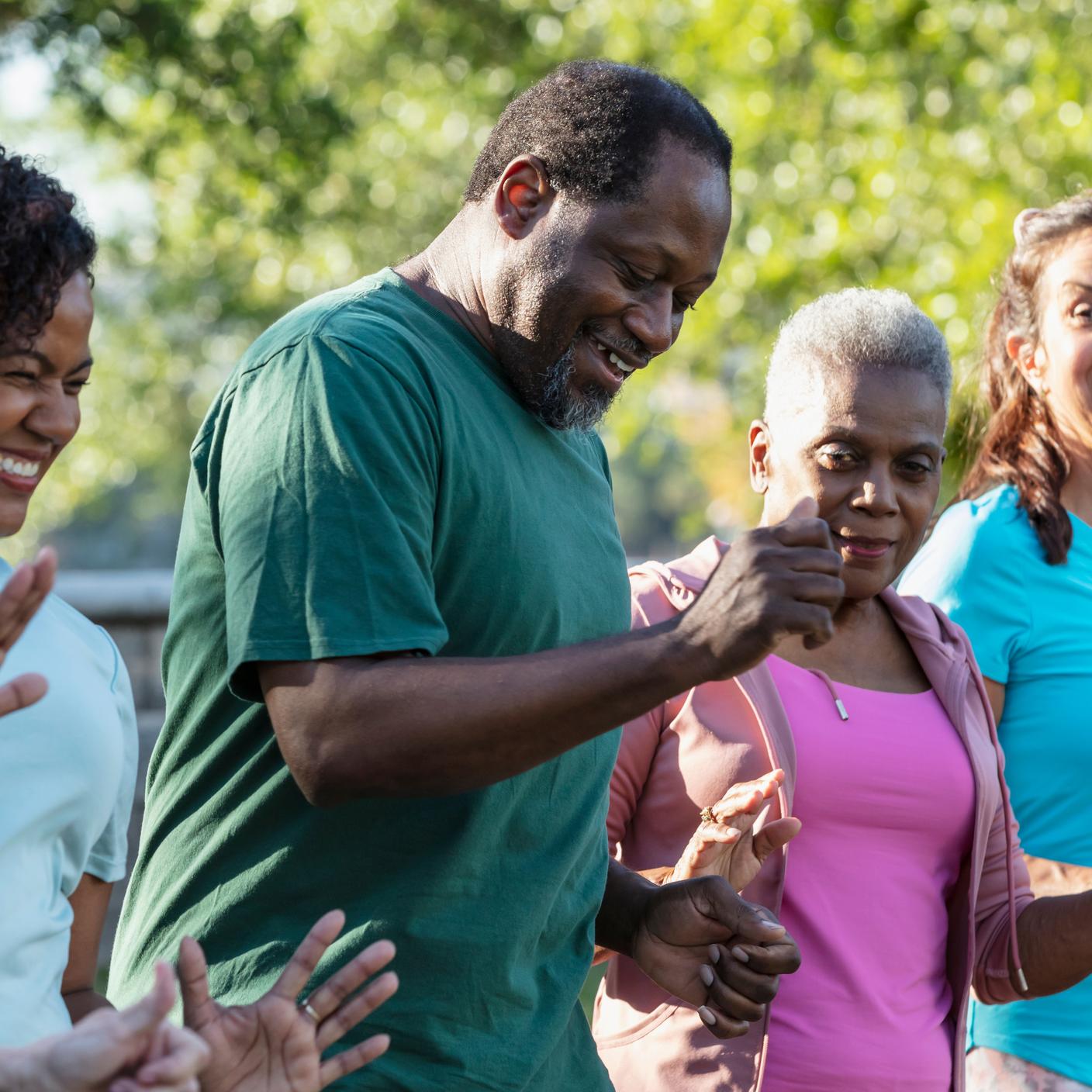 A multiracial group of five adults in a dance exercise class at the park