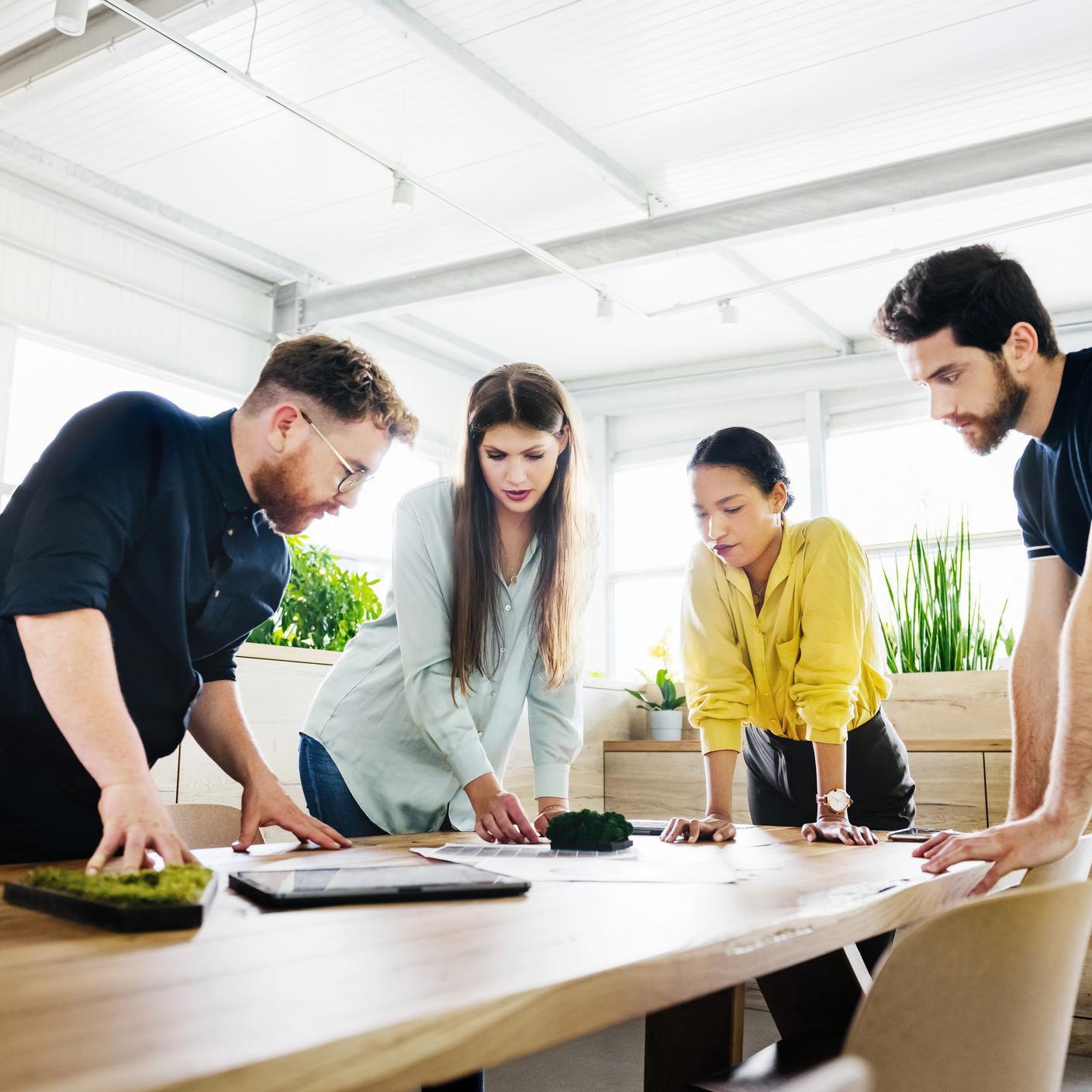 Employees huddling over some documents on a desk while consulting with each other during a business meeting