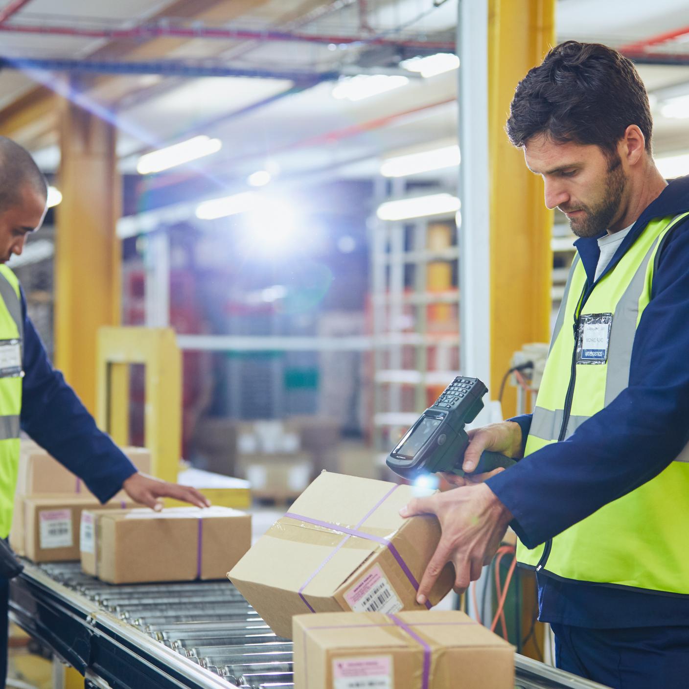 Workers scanning and processing boxes on conveyor belt in distribution warehouse