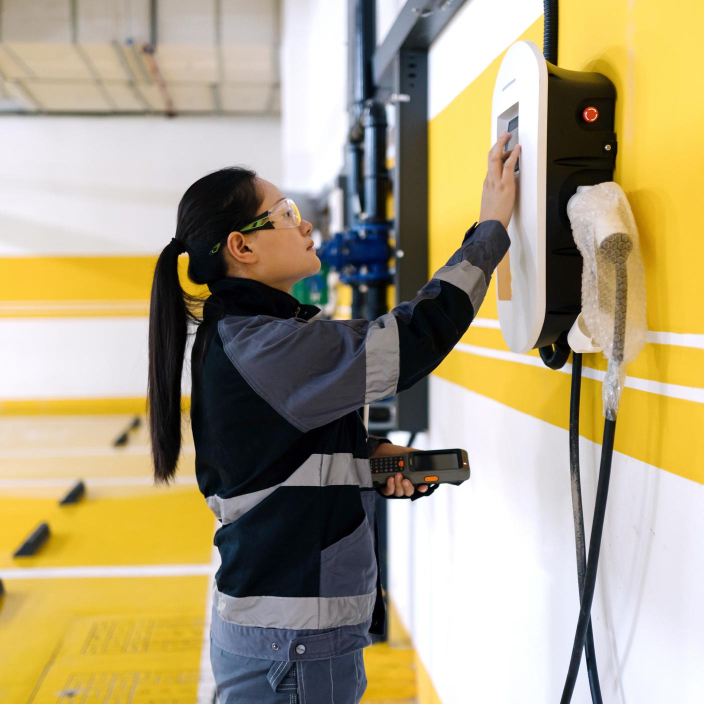 Woman engineer with EV charger, yellow background.