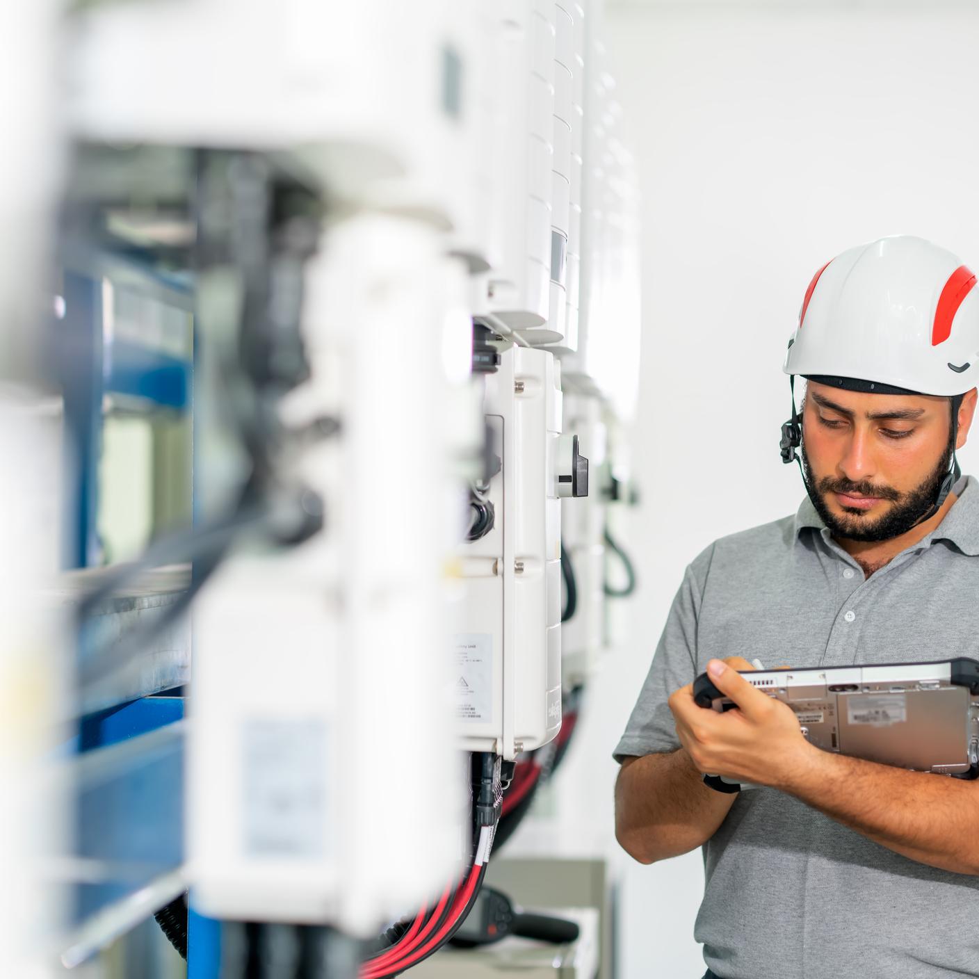 Electrician Engineers hold a tablet computer tablet to check and examination all equipment and inverter at generator control room in the solar plants.