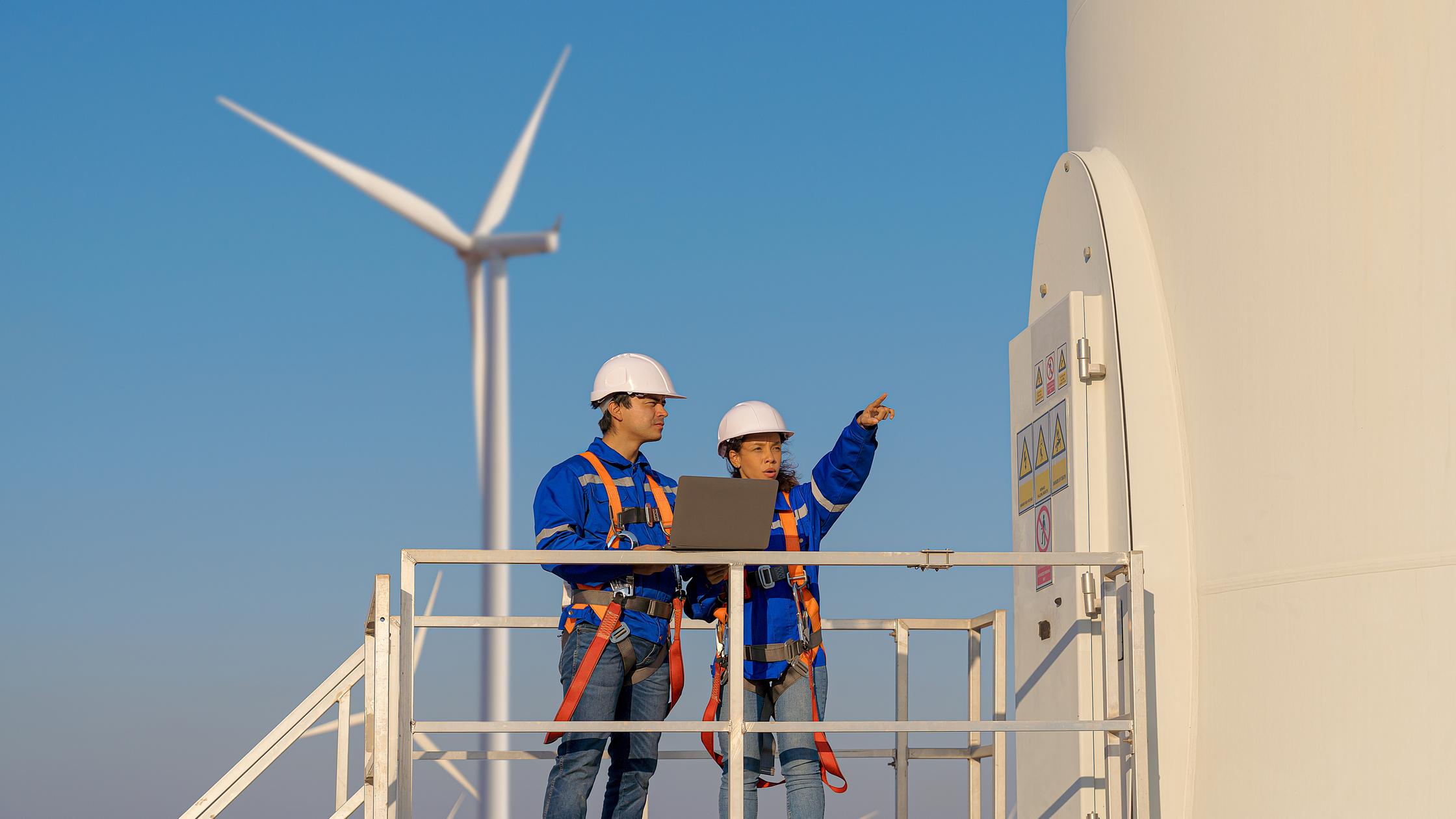 Pair of construction workers in front of windmill.