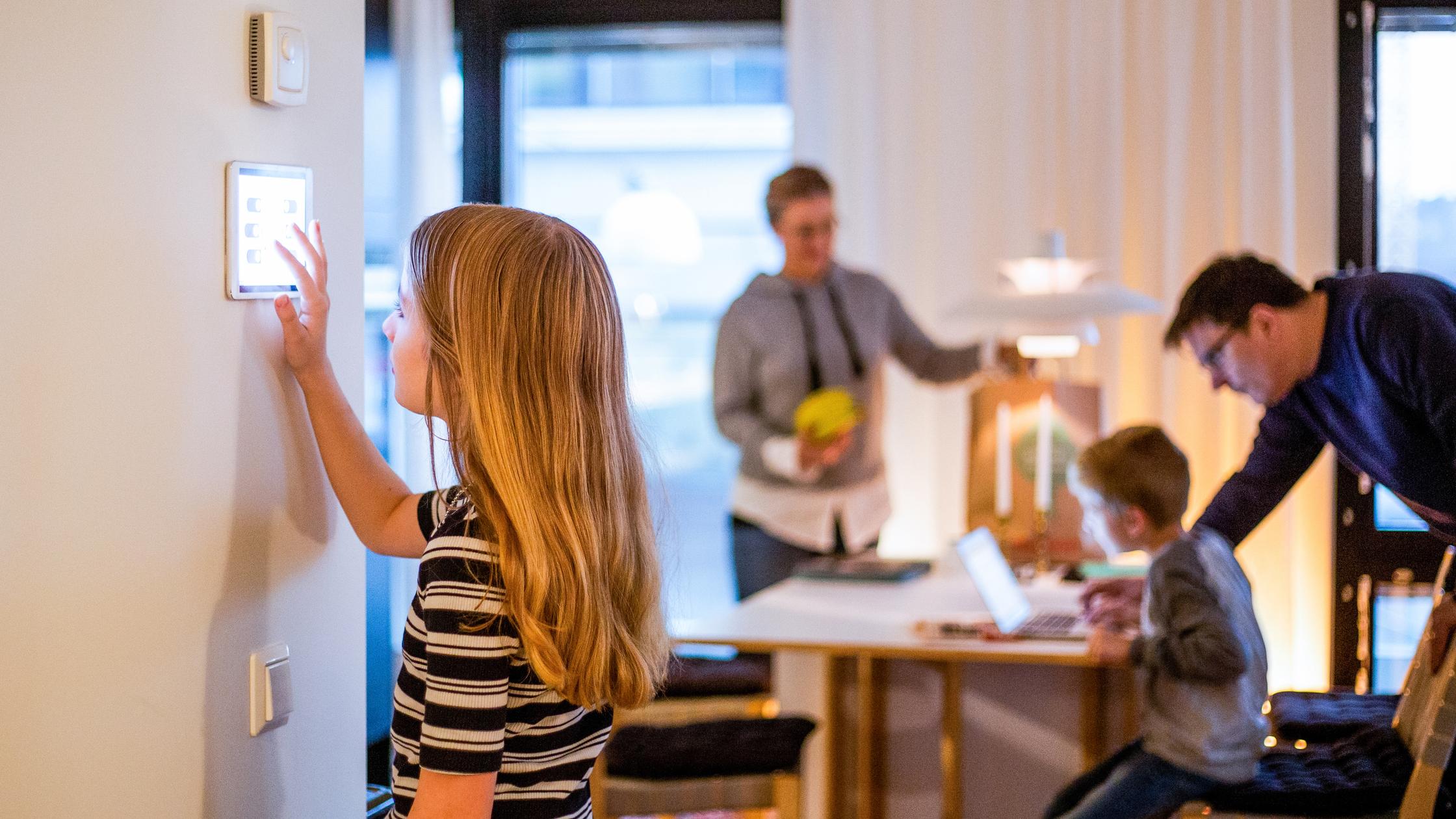 Girl using digital tablet on wall with family in background at smart home