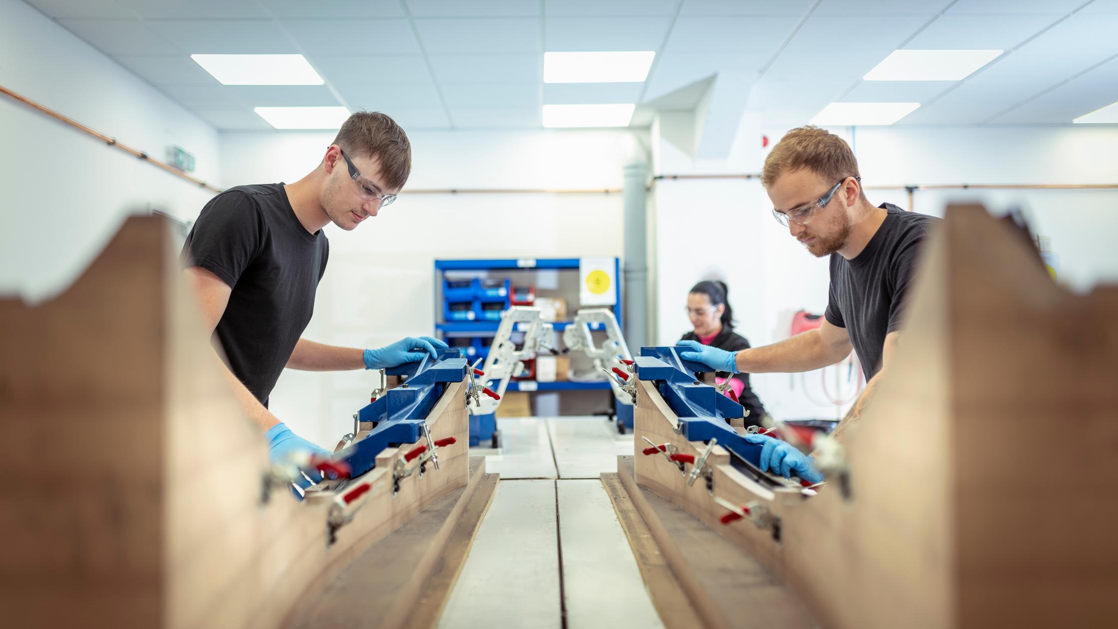 Workers on production line assembling carbon fibre parts in automotive parts factory