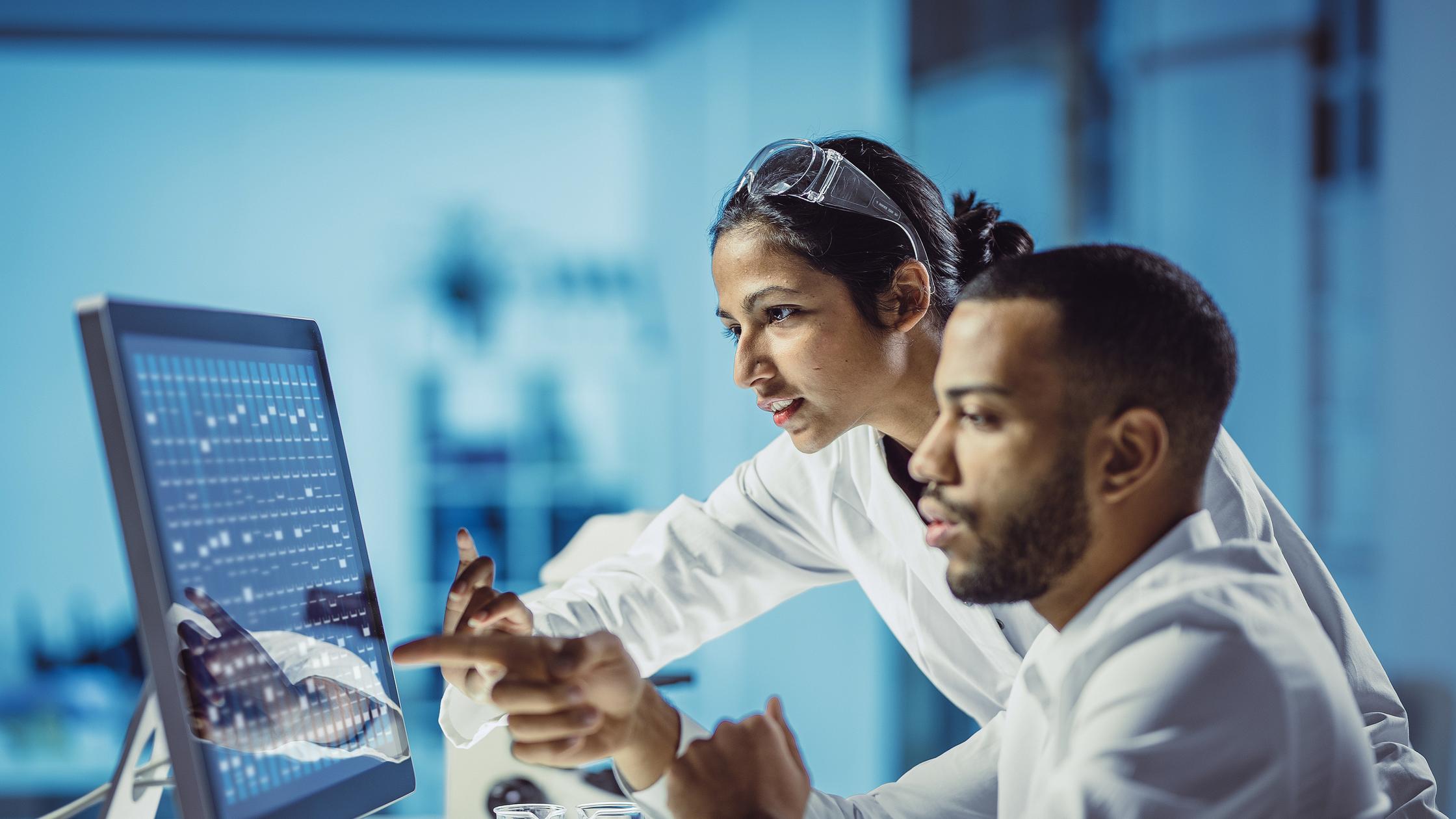 Two people working together at a desk looking at a computer screen