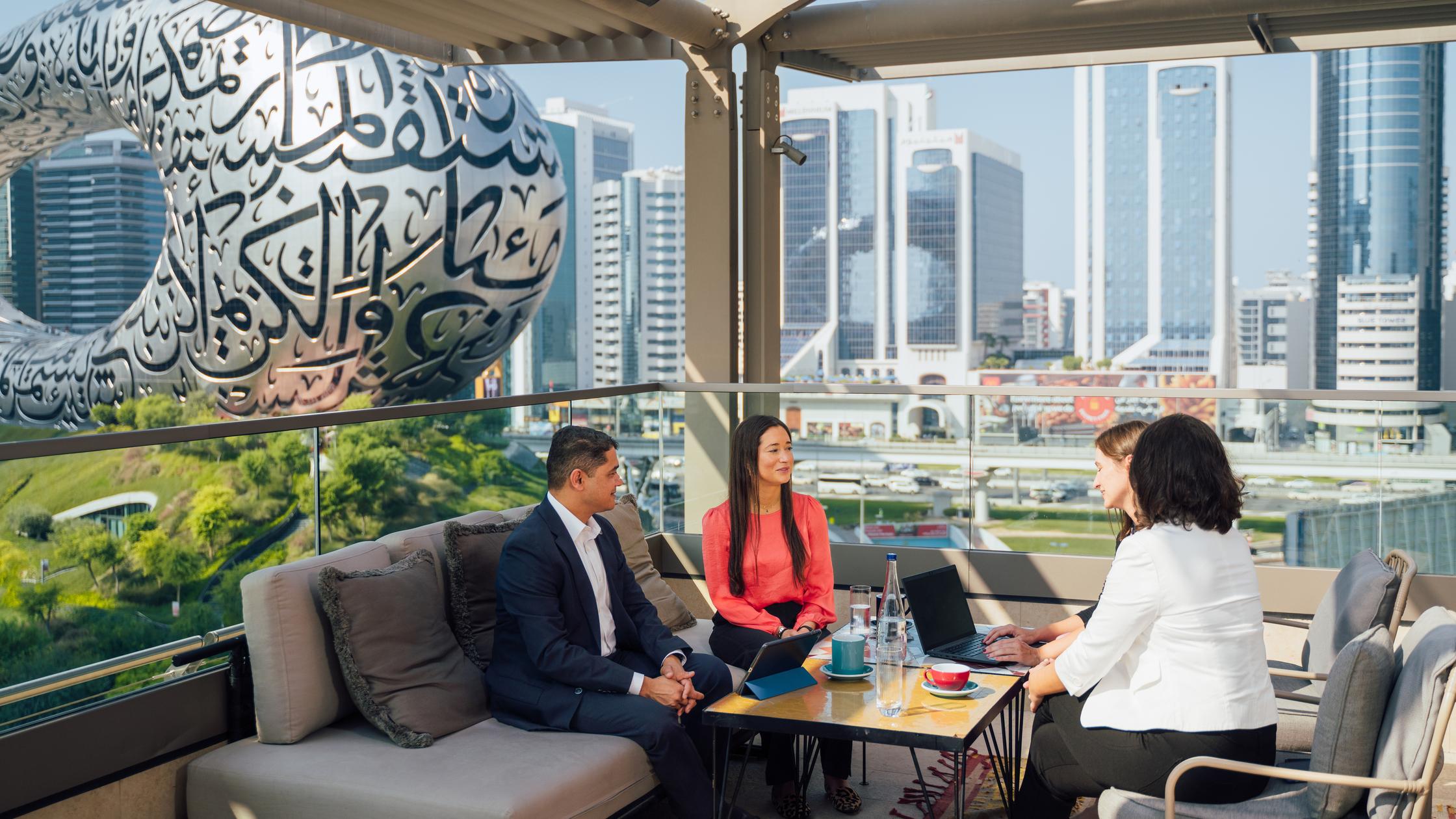 Four women and a man sitting on a rooftop with building view and discussing 