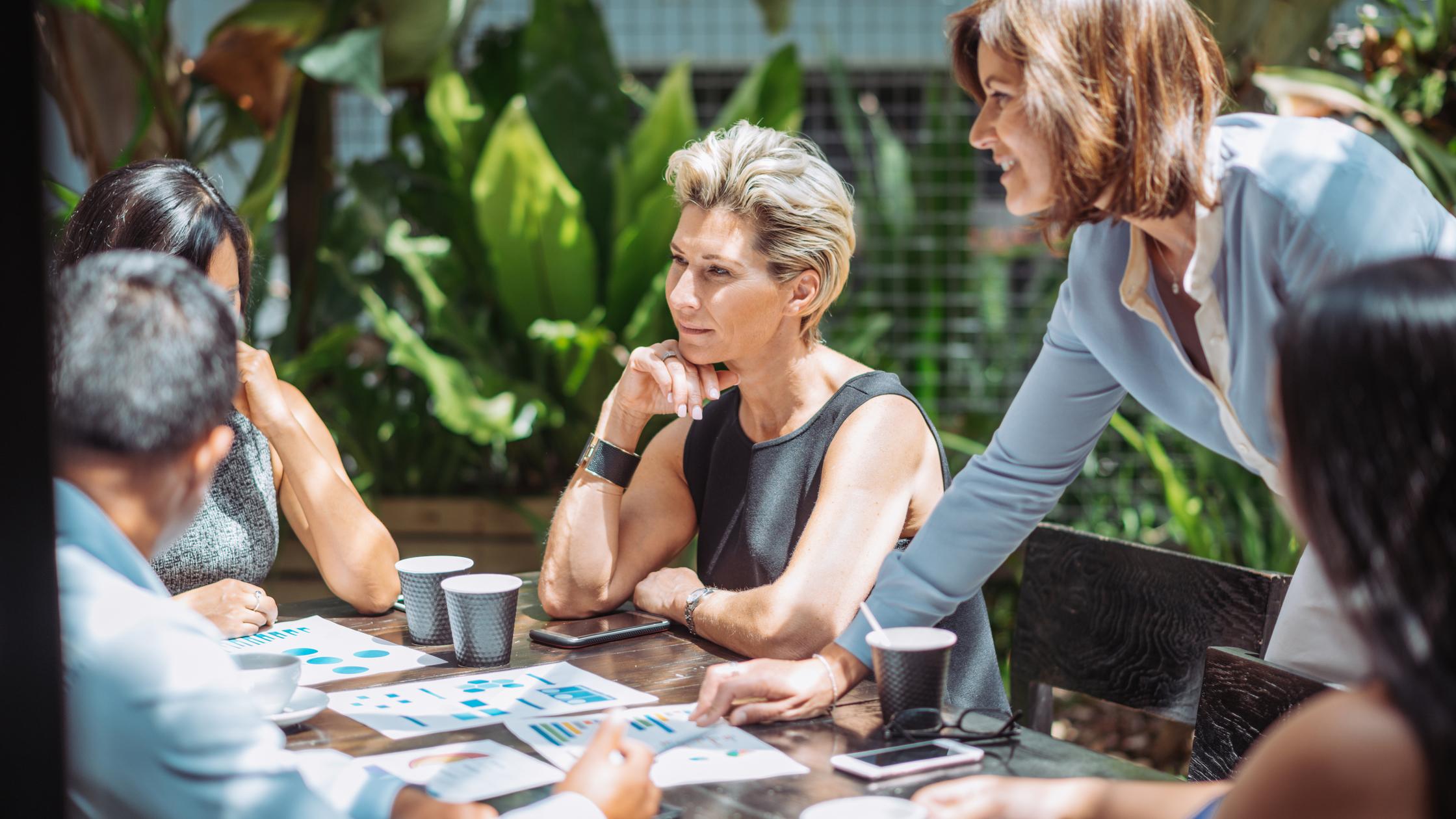 Group of professionals having a business meeting in outdoor cafe or restaurant where they discuss the investment ideas and cooperation plans while drinking coffee.