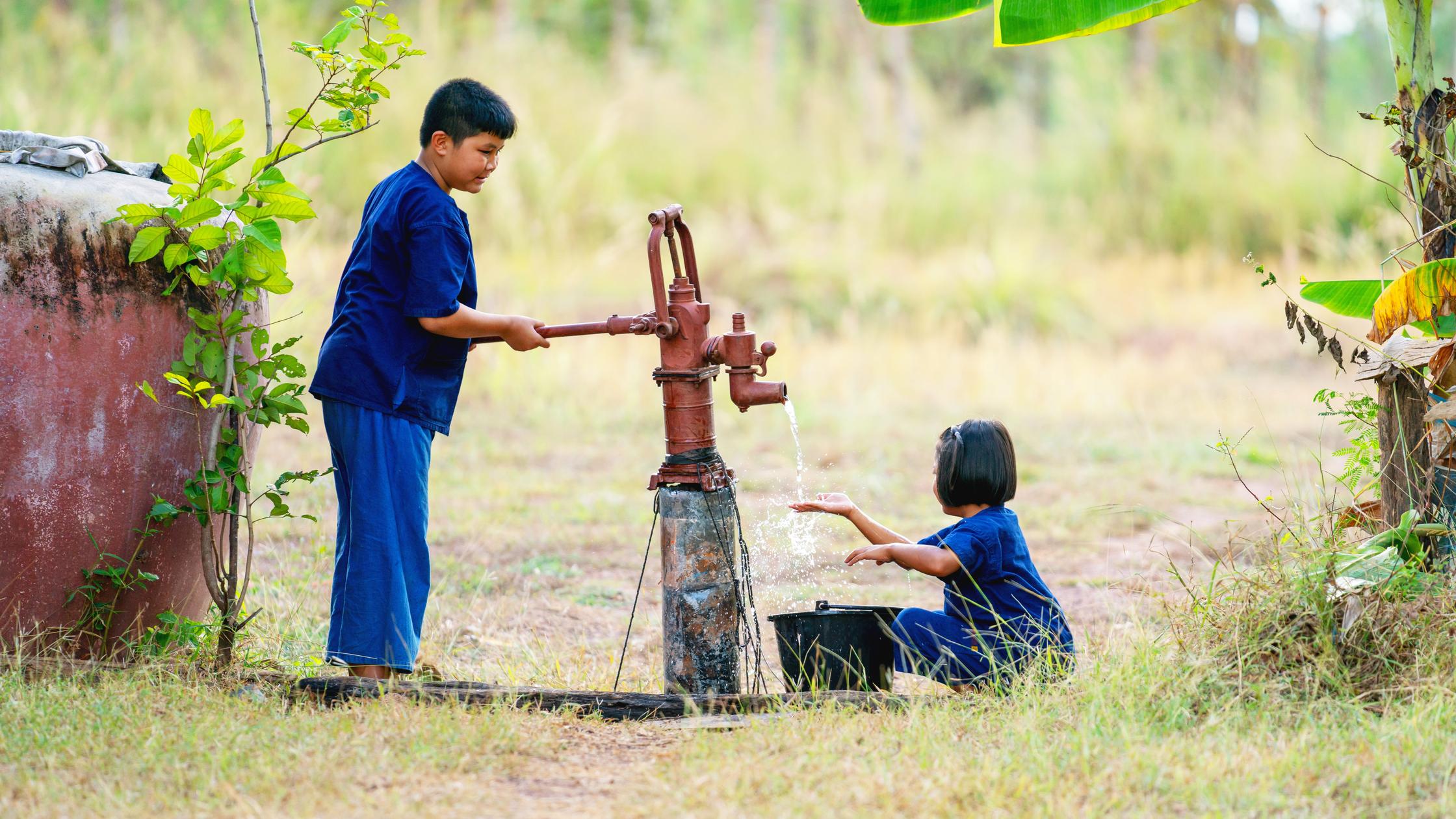 A little girl and a little boy pourring water at a fountain